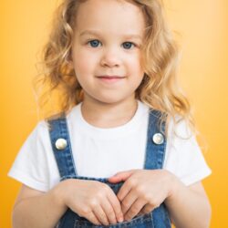 a little girl in overalls posing for a picture
